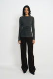 A model wearing a charcoal-heather boatneck top with a gathered waist and long sleeves, untucked over dark brown wide-leg trousers with black shoes.