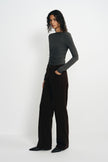 A model wearing a charcoal-heather long-sleeve top with a boat neck and gathered waist, tucked into dark brown wide-leg trousers with black pointed shoes.