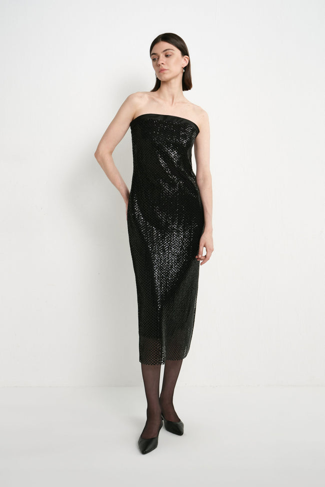 A model wearing the Rue Sophie Céleste Sequin Crochet Mesh Dress in black, featuring a strapless silhouette, sequin crochet mesh texture, and sheer midi hem, three-quarter front view.