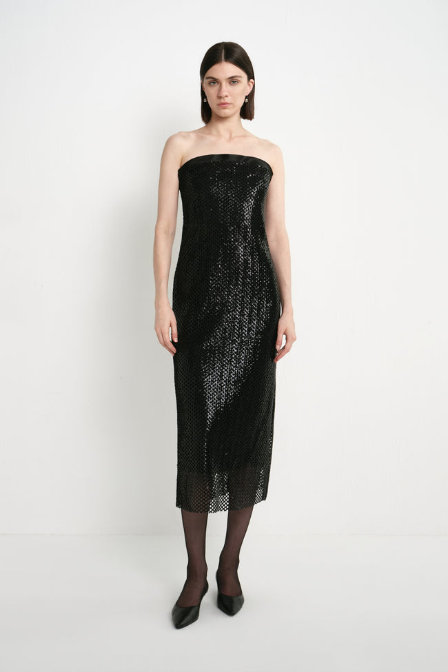 A model wearing the Rue Sophie Céleste Sequin Crochet Mesh Dress in black, a strapless midi dress with shimmering sequins, a straight neckline, and a sheer mesh hem, front view.