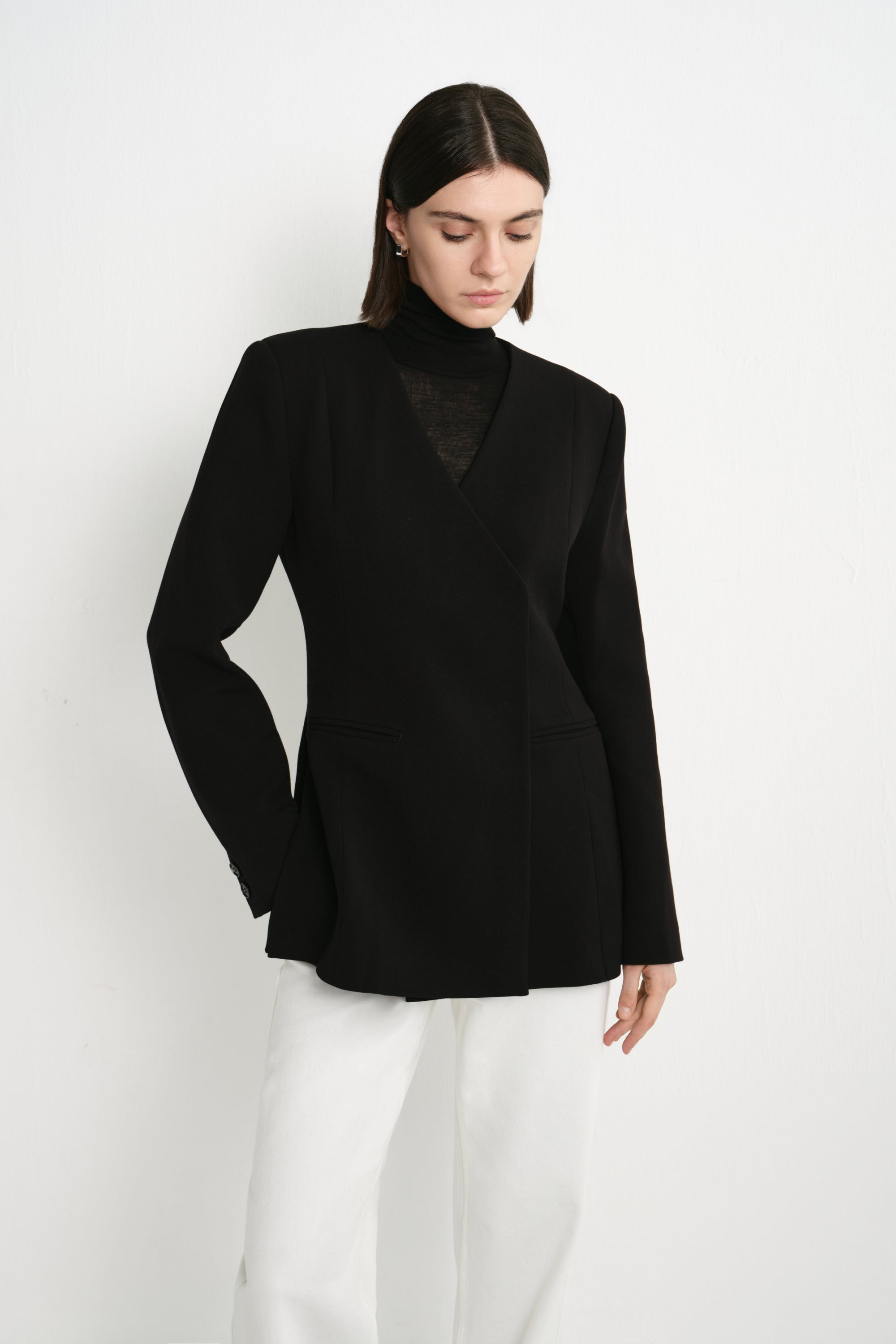 A model wearing the Rue Sophie Marion Side Slit Jacket in black, featuring a deep V-neckline, structured shoulders, welt pockets, and a defined waist, three-quarter front view.