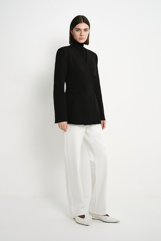 A model wearing the Rue Sophie Marion Side Slit Jacket in black with a collarless V-neckline, long sleeves, structured shoulders, and a tailored waist, three-quarter view.