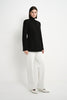 A model wearing the Rue Sophie Marion Side Slit Jacket in black with a collarless V-neckline, long sleeves, structured shoulders, and a tailored waist, three-quarter view.