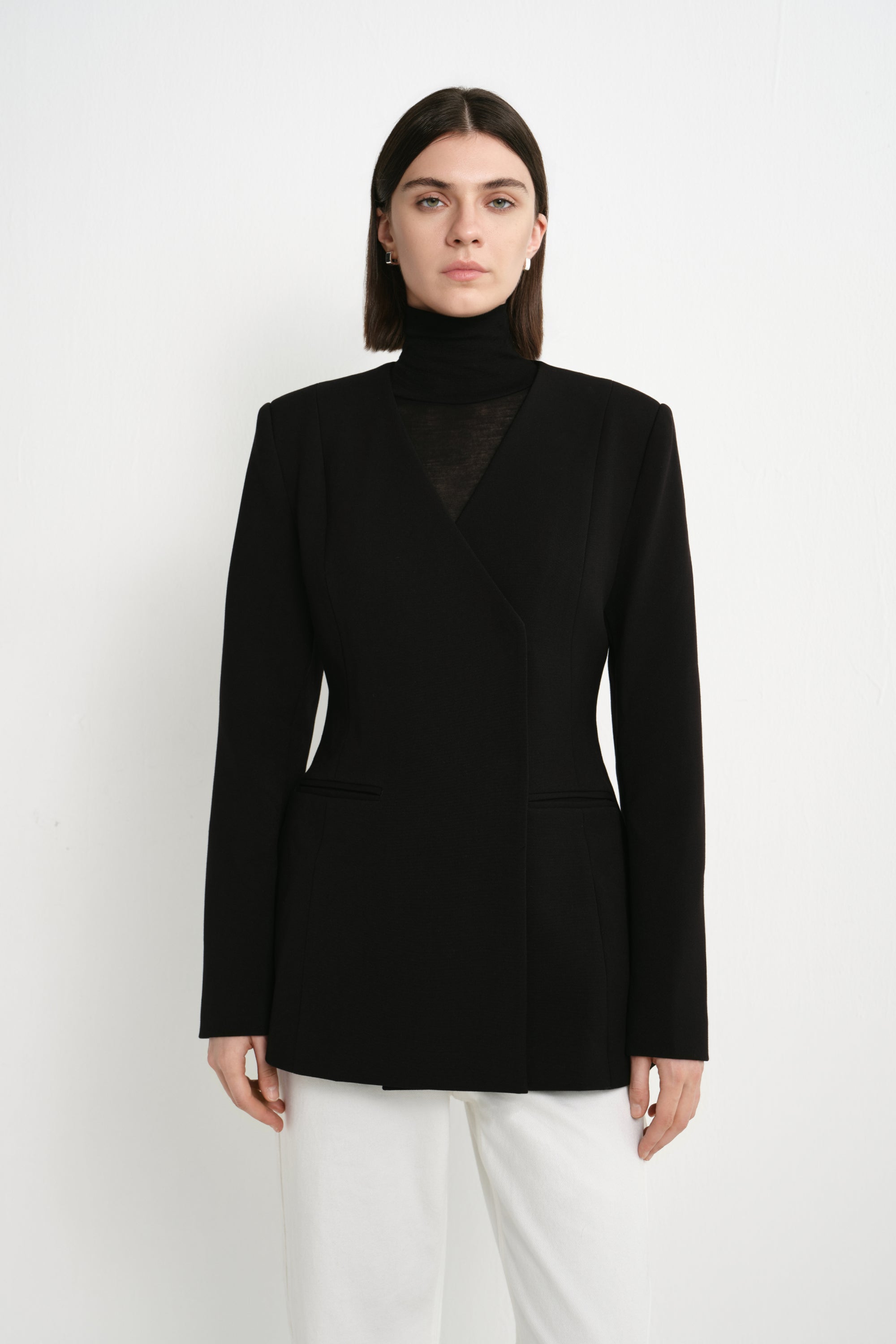 A model wearing the Rue Sophie Marion Side Slit Jacket in black, featuring structured shoulders, a collarless V-neckline, a fitted waist, and clean welt pockets, front view.