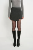 A model wearing the Rue Sophie Alina Asymmetric Mini Skirt in H. Charcoal with a structured wrap-style front panel and asymmetric hem, full-length front view.