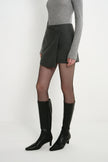 A model wearing the Rue Sophie Alina Asymmetric Mini Skirt in H. Charcoal, highlighting the angled wrap-front panel and structured mini silhouette, three-quarter view.