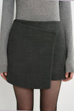 Close-up of the Rue Sophie Alina Asymmetric Mini Skirt in H. Charcoal, highlighting the overlapping wrap-style front panel, angled waistband, and structured tailoring.