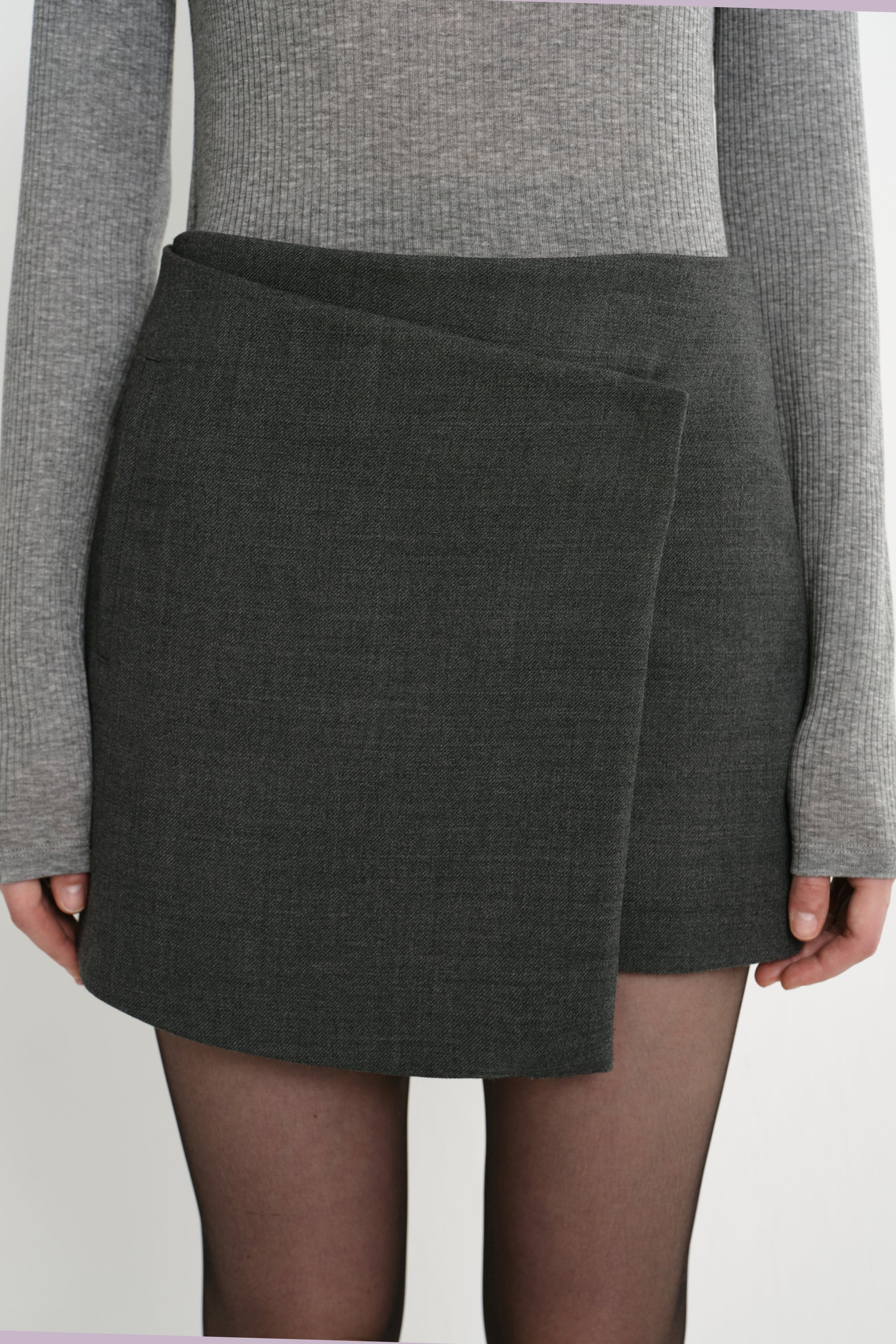 Close-up of the Rue Sophie Alina Asymmetric Mini Skirt in H. Charcoal, highlighting the overlapping wrap-style front panel, angled waistband, and structured tailoring.