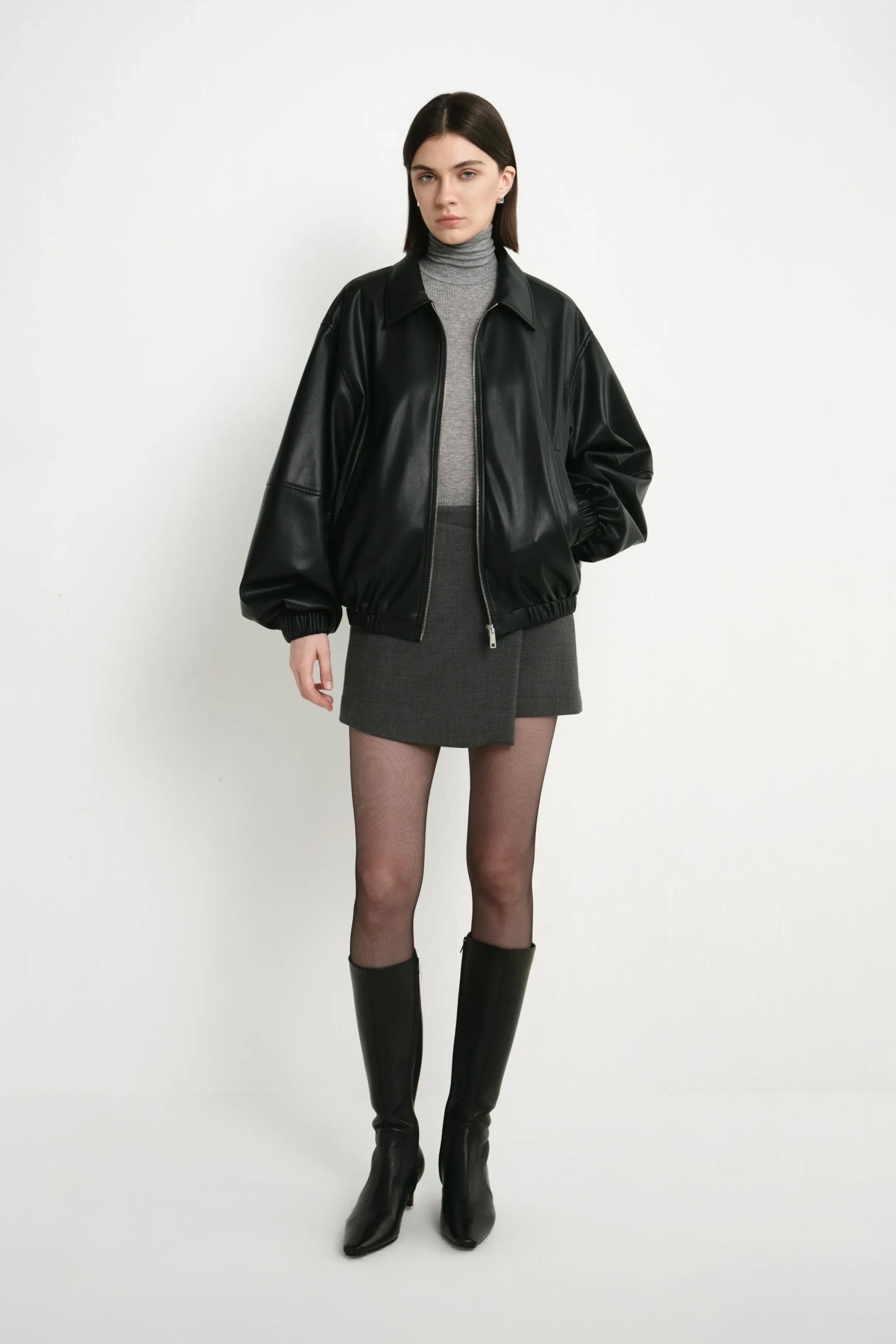 A model wearing the Rue Sophie Alina Asymmetric Mini Skirt in H. Charcoal, featuring an overlapping asymmetric front panel and clean tailored mini silhouette, front view.