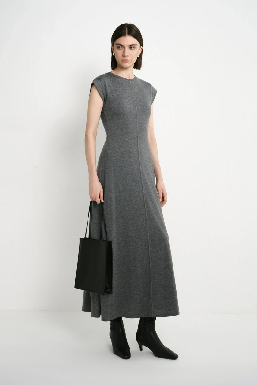 A model wearing the Rue Sophie Avi Out Stitched Dress in heather charcoal with exposed center stitching and a long flared silhouette, three-quarter front view.