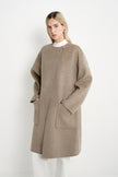 A model wearing a Rue Sophie oak collarless long coat with oversized patch pockets and a relaxed silhouette, three-quarter view.