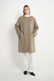 A model wearing a Rue Sophie oak collarless long coat with drop shoulders, front patch pockets, and a straight relaxed silhouette, full-length front view.