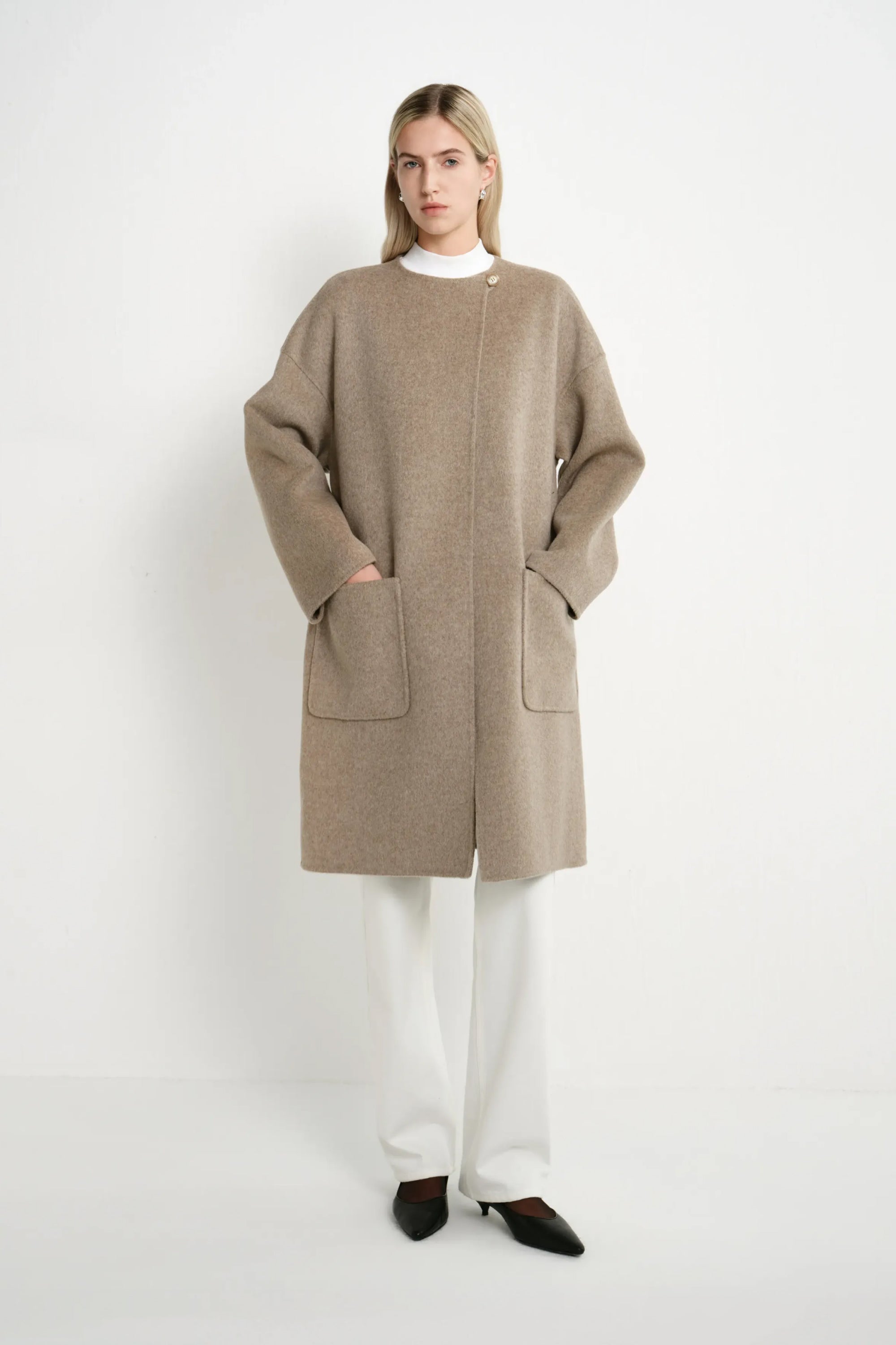 A model wearing a Rue Sophie oak collarless long coat with drop shoulders, front patch pockets, and a straight relaxed silhouette, full-length front view.