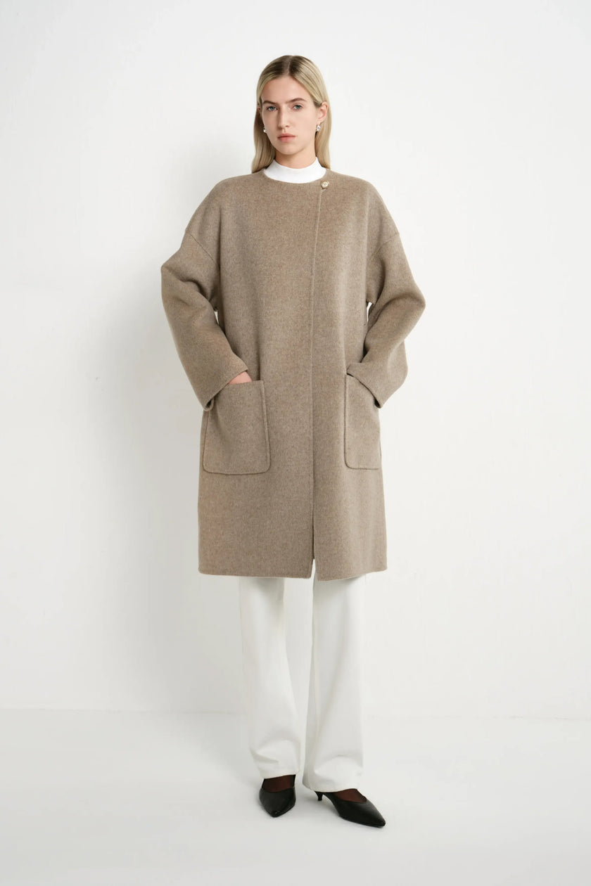 A model wearing a Rue Sophie oak collarless long coat with drop shoulders, front patch pockets, and a straight relaxed silhouette, full-length front view.