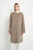 A model wearing a Rue Sophie oak collarless long coat with a single neck button, concealed front closure, and oversized patch pockets, front view.