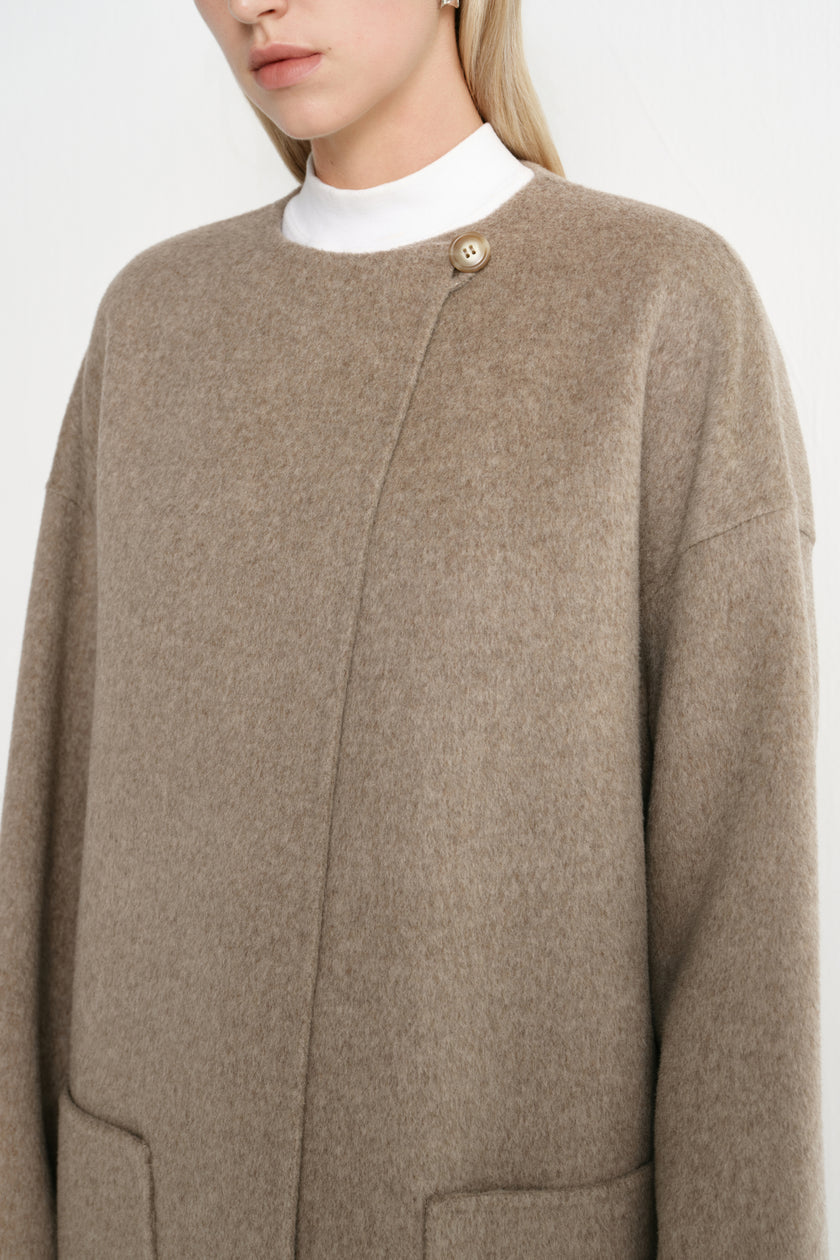 Close-up of a Rue Sophie oak collarless long coat featuring a single neck button, concealed front closure, drop shoulder construction, and soft brushed texture.