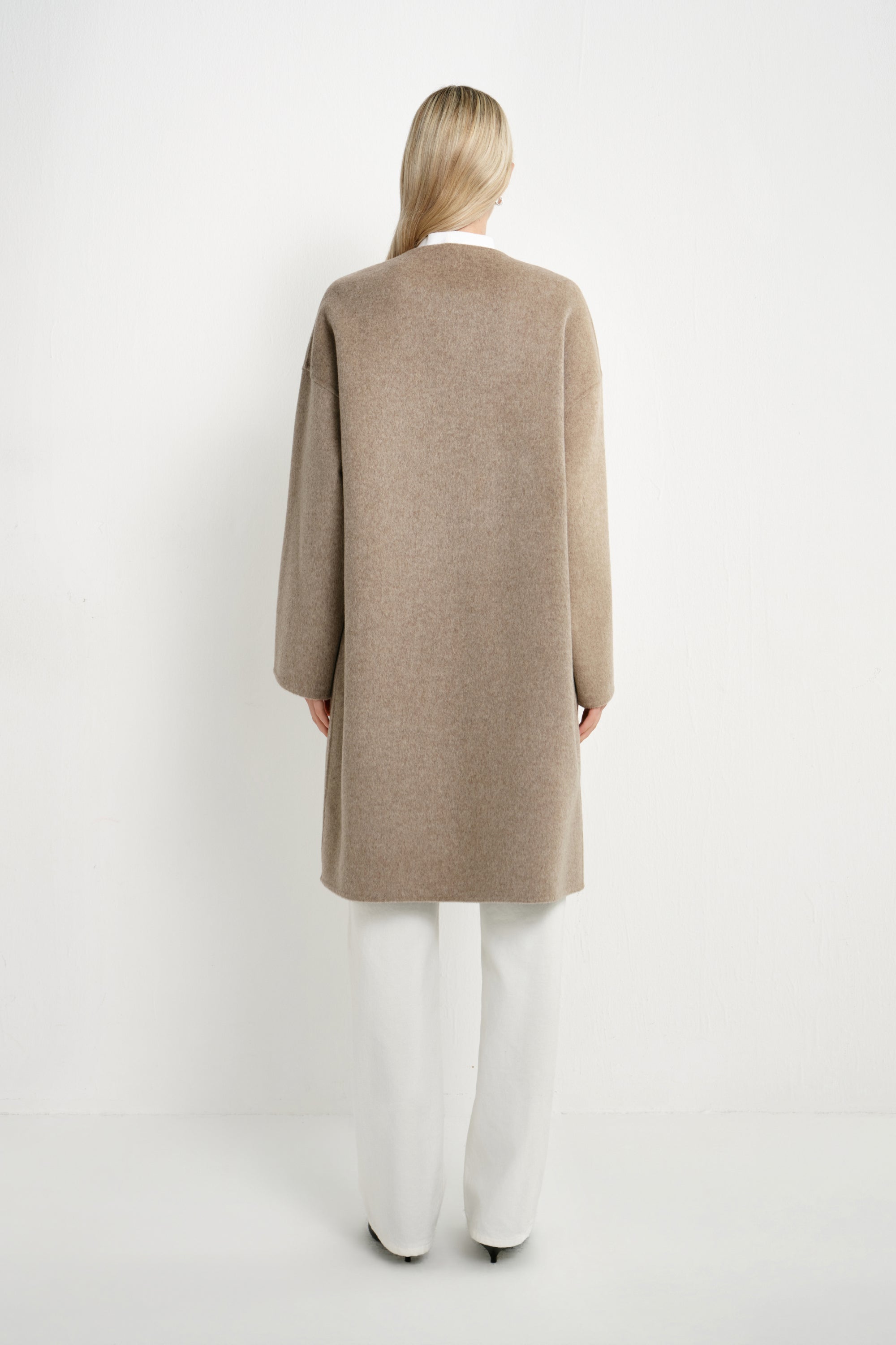 Back view of a model wearing a Rue Sophie oak collarless long coat with dropped shoulders, wide sleeves, and a clean straight silhouette.
