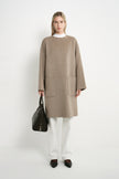 A model wearing a Rue Sophie oak collarless long coat with a clean front closure, oversized patch pockets, and relaxed drop shoulders, front view.