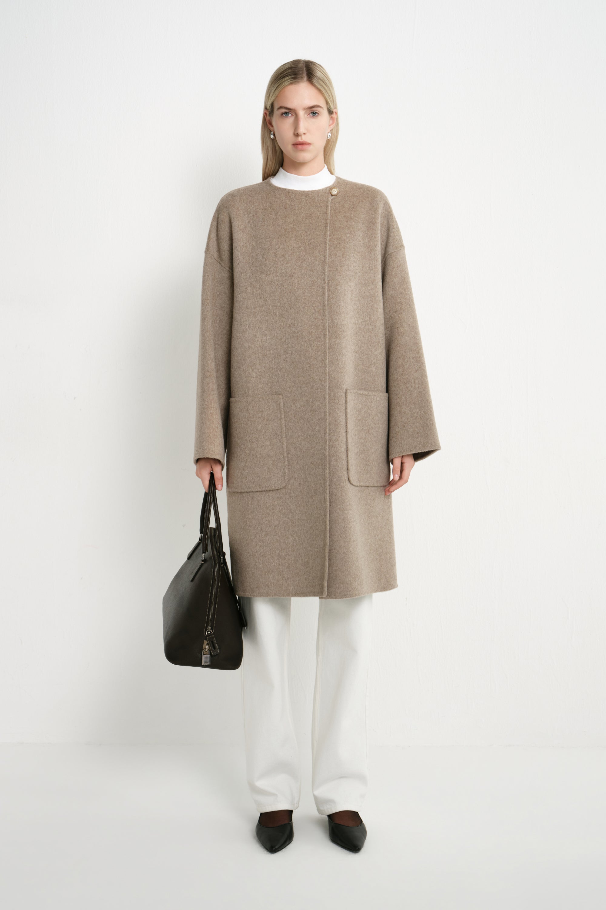 A model wearing a Rue Sophie oak collarless long coat with a clean front closure, oversized patch pockets, and relaxed drop shoulders, front view.