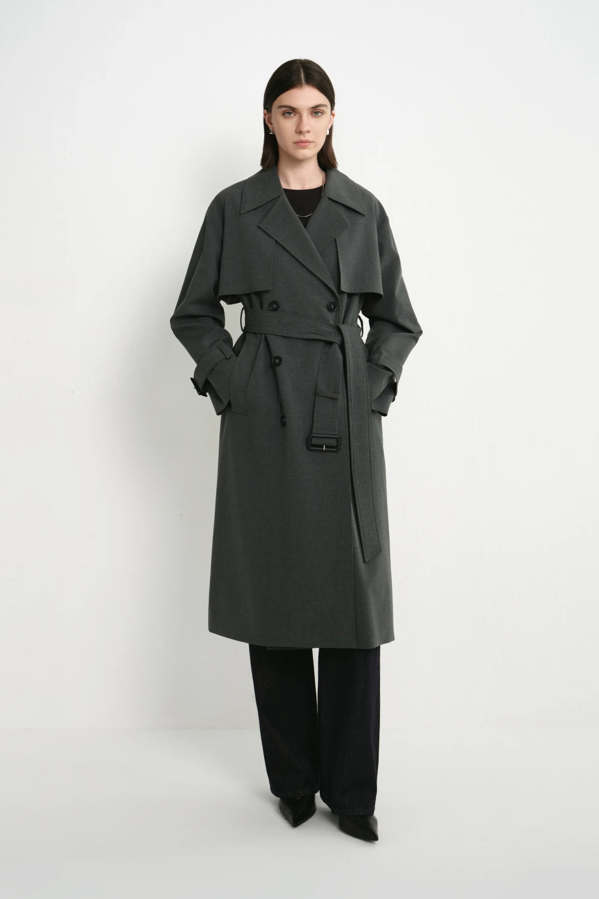 A model wearing the Rue Sophie Gavin Trench Coat in H. Charcoal with wide lapels, double-breasted buttons, a belted waist, and a relaxed tailored fit, three-quarter front view.
