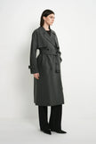 A model wearing the Rue Sophie Gavin Trench Coat in H. Charcoal, featuring a structured collar, double-breasted closure, waist belt, and long tailored silhouette, side view.