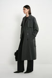 A model wearing the Rue Sophie Gavin Trench Coat in H. Charcoal, featuring wide lapels, a double-breasted front, belted waist, side pockets, and a relaxed long silhouette, three-quarter side view.