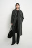 A model wearing the Rue Sophie Gavin Trench Coat in H. Charcoal, featuring a double-breasted front, wide lapels, belted waist, and a relaxed long silhouette, front view.
