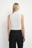 A woman shown from the back wearing a sleeveless white mock-neck top and dark charcoal pants against a plain white studio background.