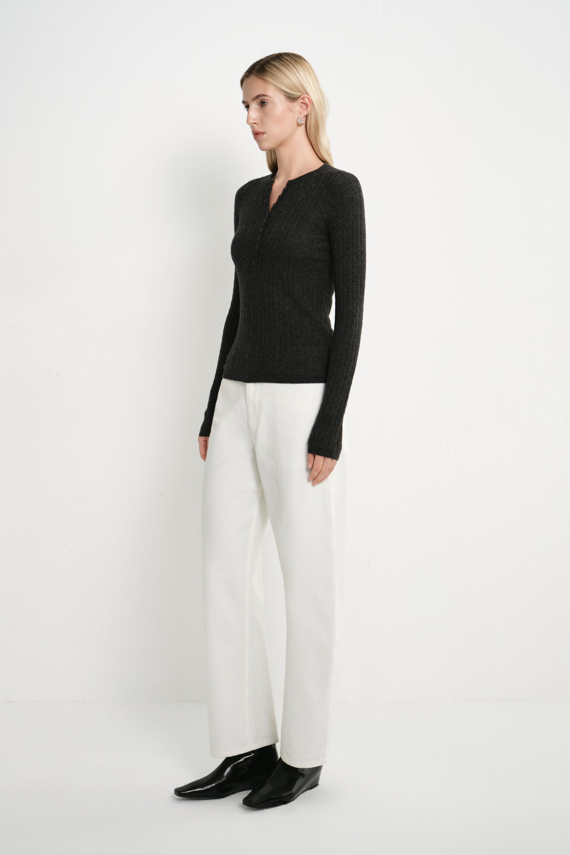 A model wearing the Rue Sophie Richie Button Up Cable Sweater in heather grey with long sleeves, a fitted waist, and textured cable knit, side view.