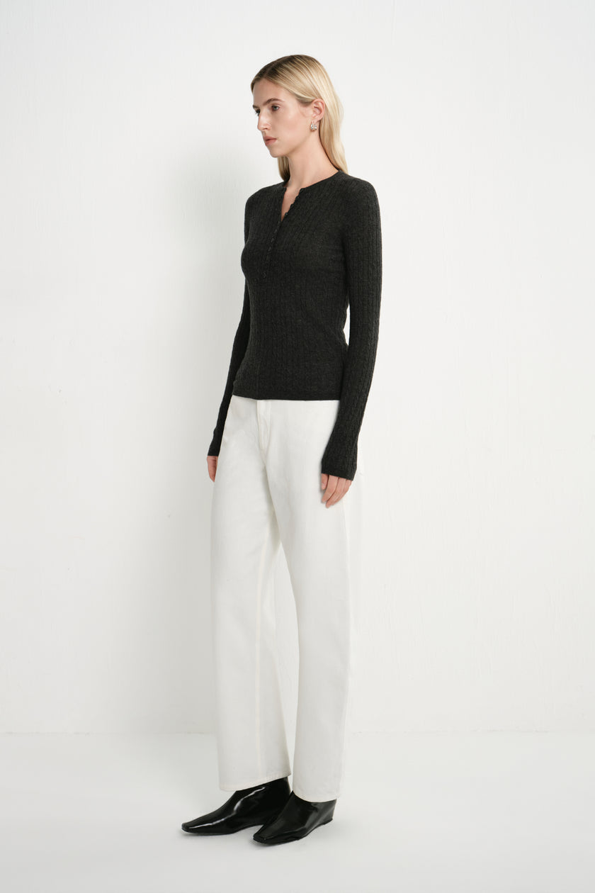 A model wearing the Rue Sophie Richie Button Up Cable Sweater in heather grey with long sleeves, a fitted waist, and textured cable knit, side view.