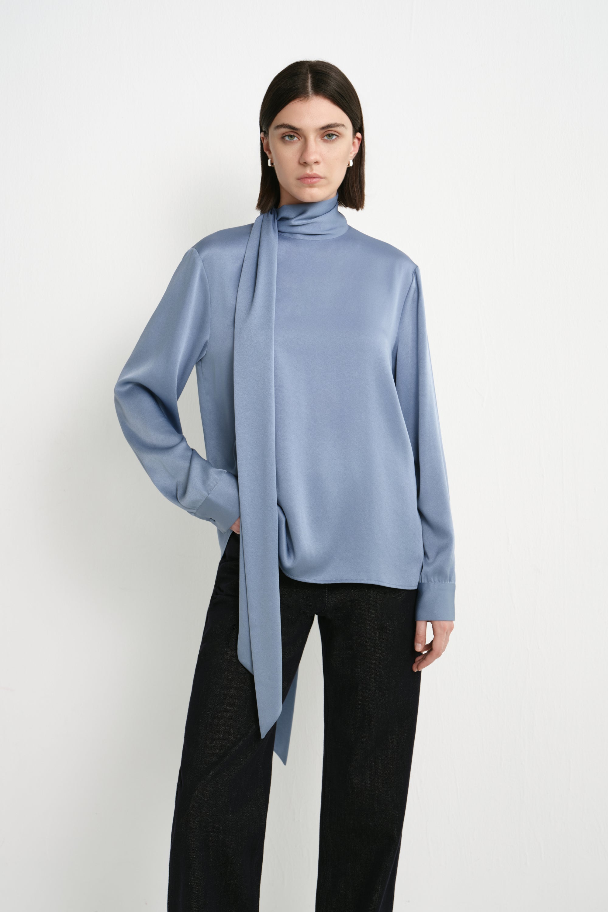 A model wearing the Rue Sophie Samara Tie Neck Top in Harbour with a high scarf neckline, elongated tie detail, buttoned cuffs, and a softly draped silhouette, front view.