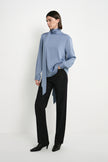 A model wearing the Rue Sophie Samara Tie Neck Top in Harbour with a high draped neckline, long scarf tie, and relaxed flowing silhouette, three-quarter front view.