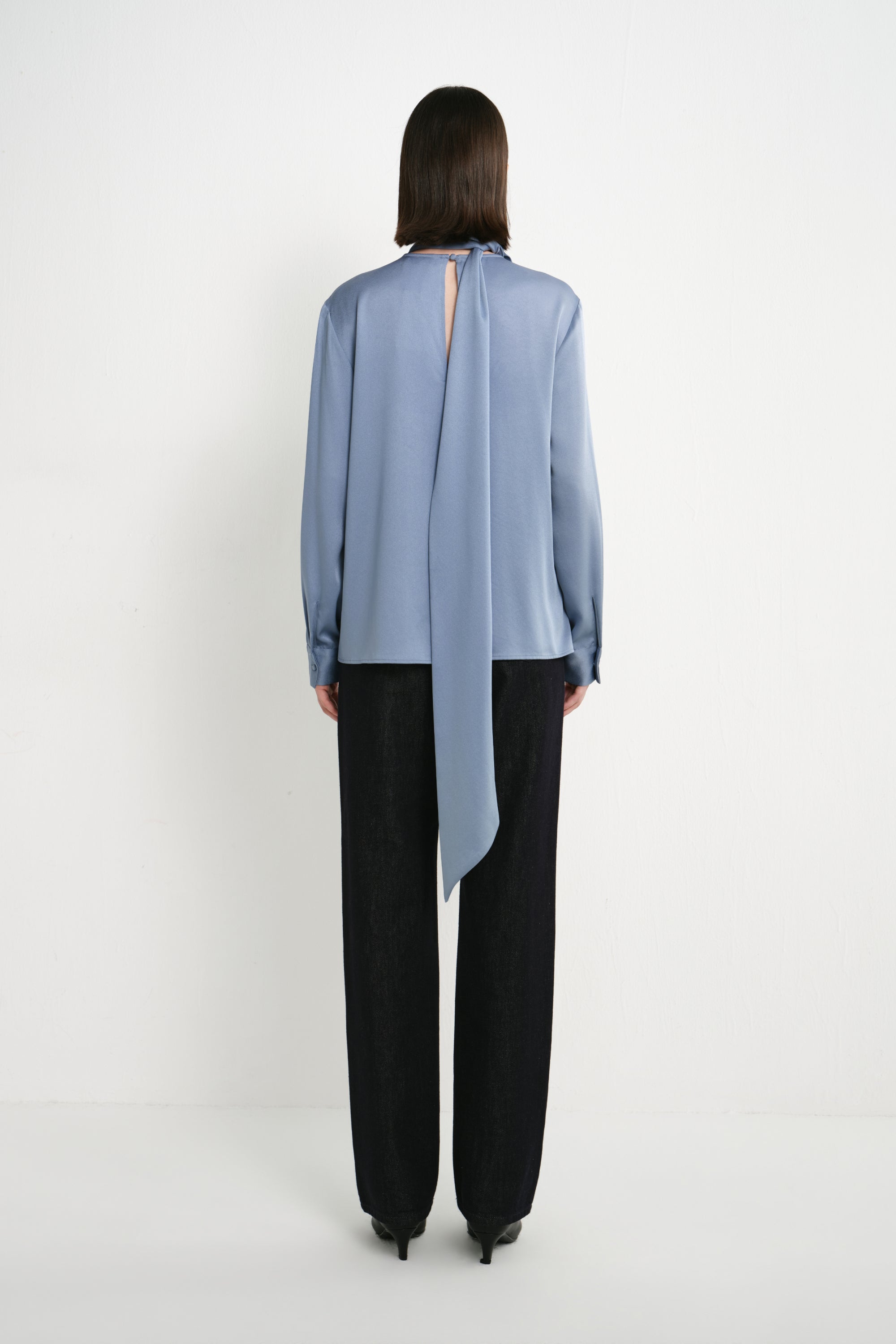 Back view of a model wearing the Rue Sophie Samara Tie Neck Top in Harbour, featuring a back keyhole opening, long scarf tie, and relaxed long-sleeve silhouette.