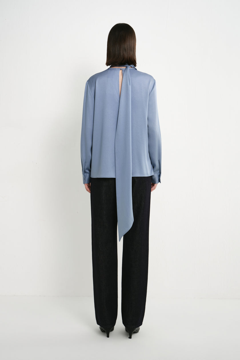 Back view of a model wearing the Rue Sophie Samara Tie Neck Top in Harbour, featuring a back keyhole opening, long scarf tie, and relaxed long-sleeve silhouette.