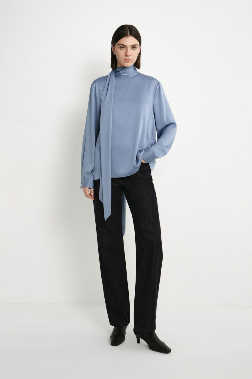 A model wearing the Rue Sophie Samara Tie Neck Top in Harbour with a high scarf neckline, long asymmetric tie, buttoned cuffs, and relaxed draped shape, full-length front view.