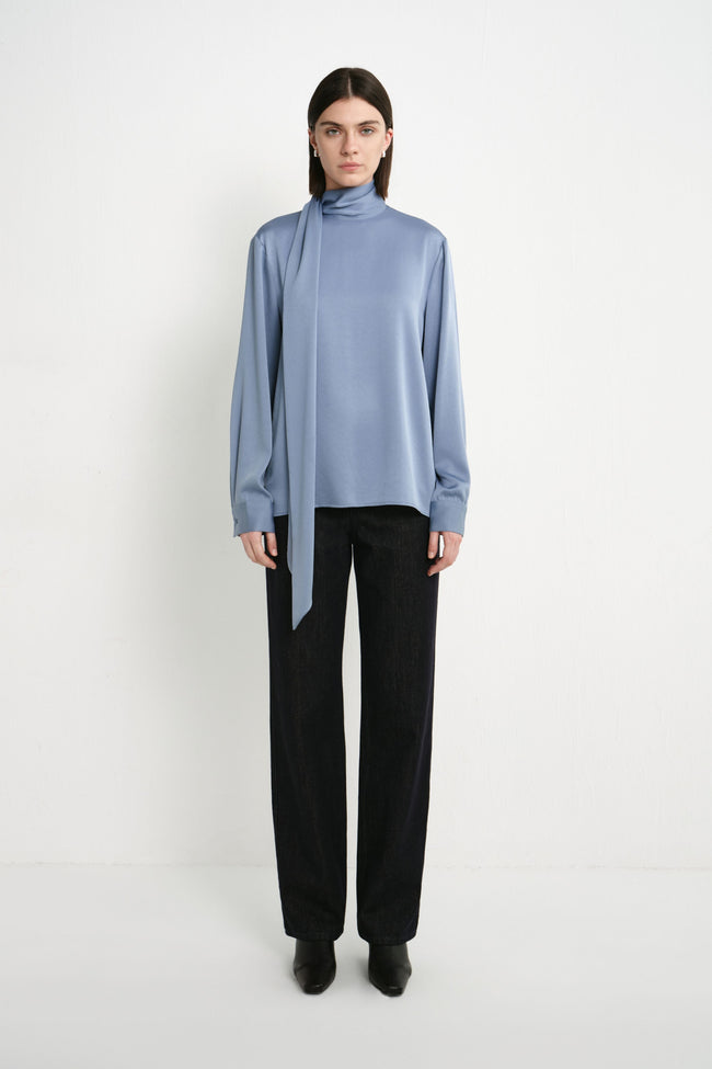 A model wearing the Rue Sophie Samara Tie Neck Top in Harbour, featuring a high scarf neckline, long draped tie, long sleeves, and a relaxed fluid silhouette, front view.