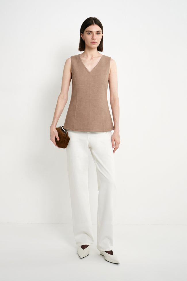 A model wearing the Rue Sophie Jesi V-Neck Top in Oak with white trousers, featuring a sleeveless V-neck design and fitted tailored silhouette, full front view.