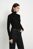 Angled view of Rue Sophie’s Lila Drape Scarf Jersey Top in Black, featuring a high neckline, softly draped chest detail and fitted long sleeves.