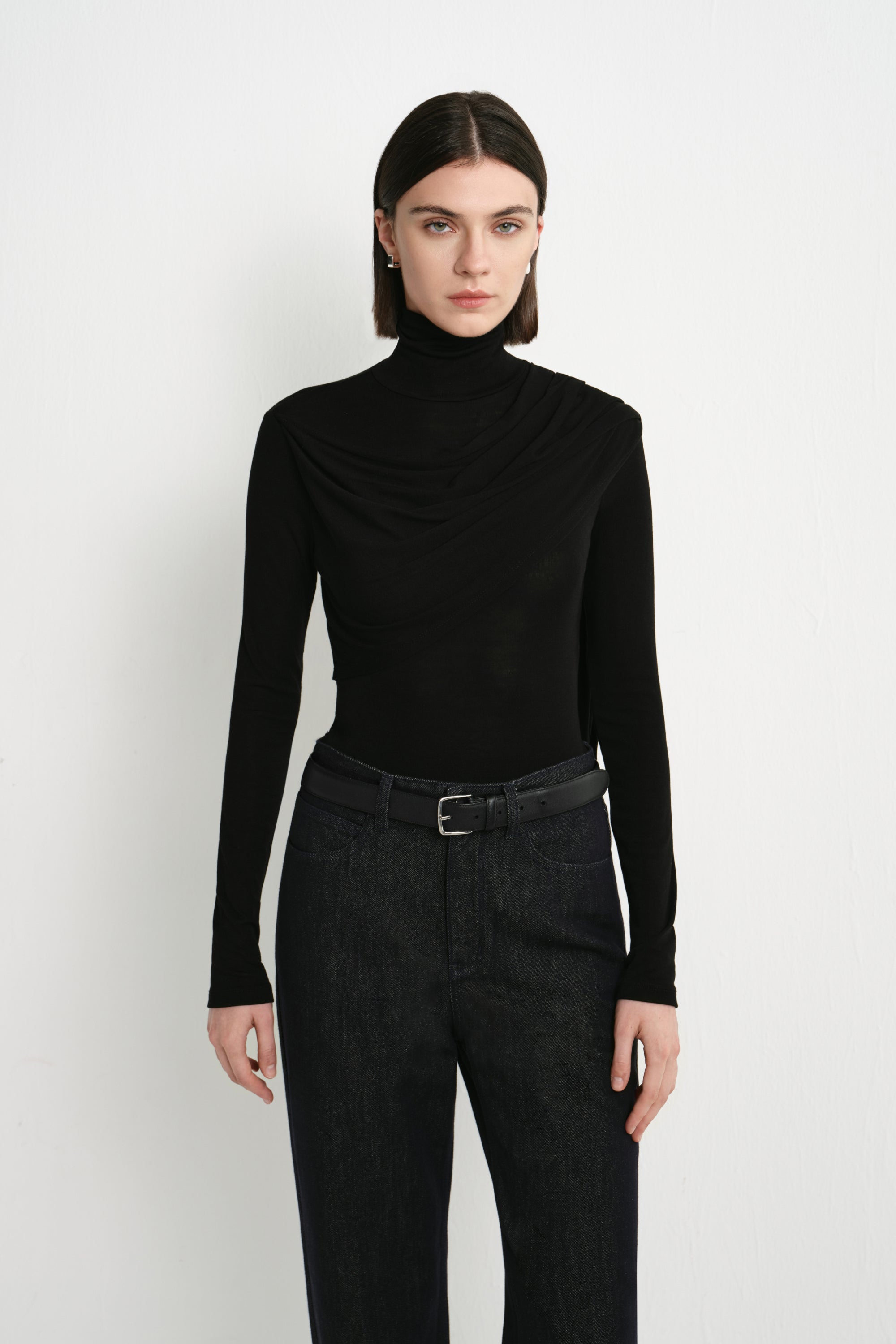 Front view of Rue Sophie’s Lila Drape Scarf Jersey Top in Black, featuring a high neckline, asymmetric draping across the chest and a close-fitting silhouette.