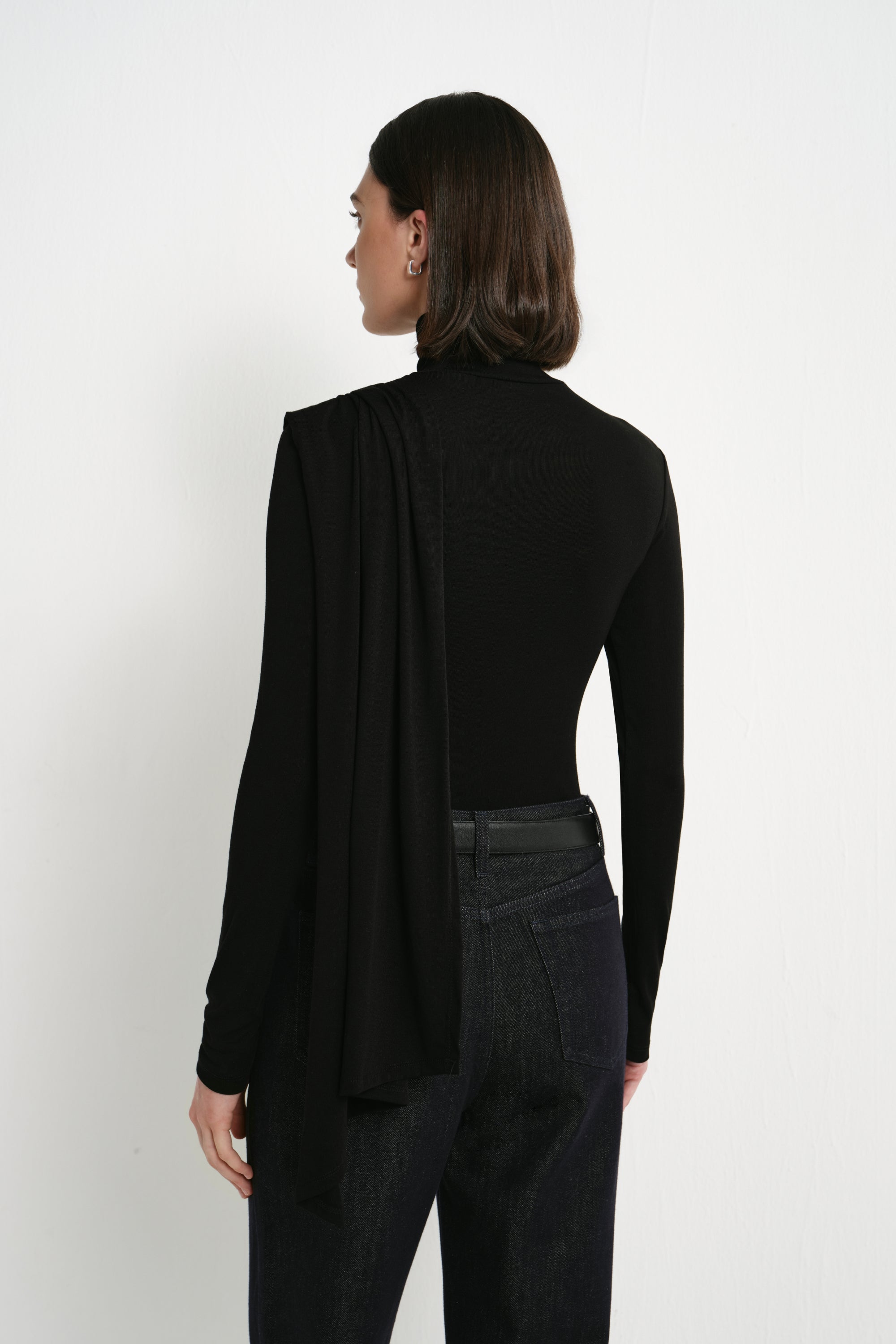 Back view of Rue Sophie’s Lila Drape Scarf Jersey Top in Black, showing the fitted long-sleeve silhouette and elongated draped scarf panel falling from the shoulder.