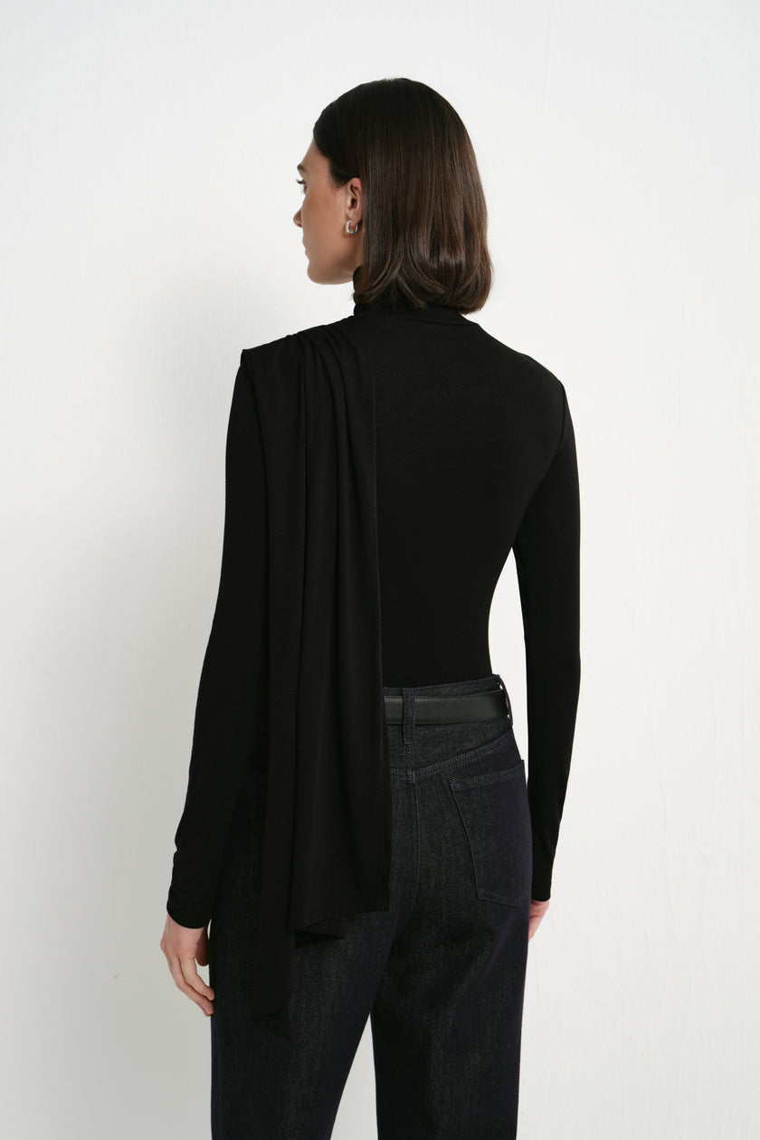 Back view of Rue Sophie’s Lila Drape Scarf Jersey Top in Black, showing the fitted long-sleeve silhouette and elongated draped scarf panel falling from the shoulder.