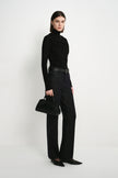 A model wearing Rue Sophie’s Lila Drape Scarf Jersey Top in Black with dark jeans and a black handbag, showing the fitted silhouette and asymmetric draped neckline.