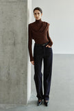 A model wearing a dark brown draped turtleneck top with an extended asymmetric shoulder panel, styled with a light beige A-line midi skirt and black pointed pumps.