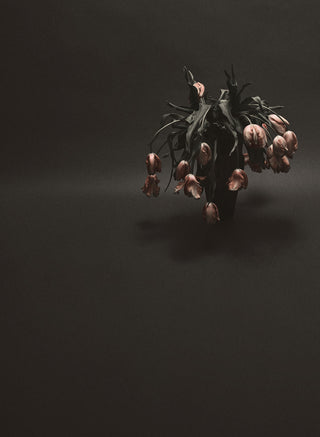 A vase with dead flowers in front of a grey background 
