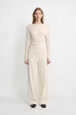 A model wearing Rue Sophie’s Talia Wide Leg Corduroy Pant in Winter White, styled with an ivory draped long-sleeve top and black square-toe shoes. The full-length view highlights the relaxed wide-leg silhouette and fine vertical corduroy texture.