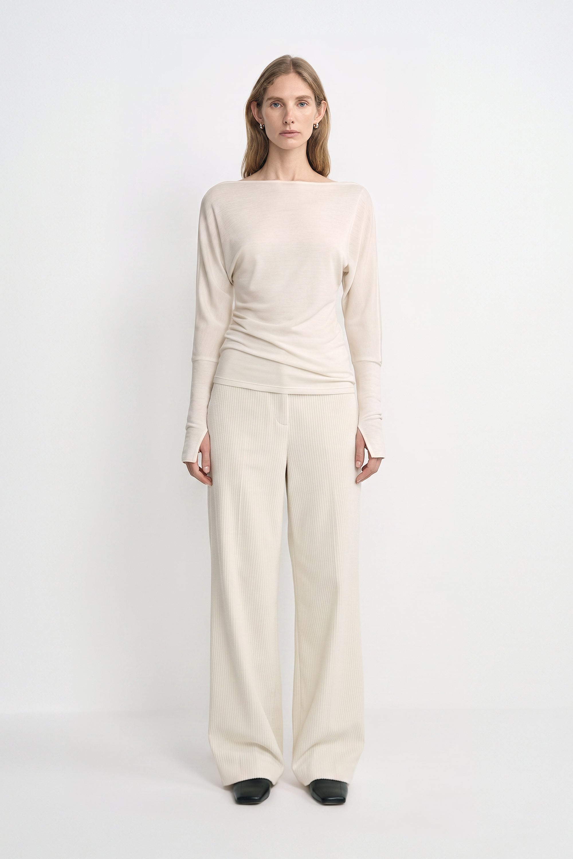 A model wearing Rue Sophie’s Talia Wide Leg Corduroy Pant in Winter White, styled with an ivory draped long-sleeve top and black square-toe shoes. The full-length view highlights the relaxed wide-leg silhouette and fine vertical corduroy texture.