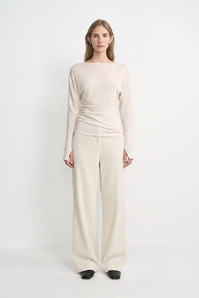 A model wearing Rue Sophie’s Talia Wide Leg Corduroy Pant in Winter White, styled with an ivory draped long-sleeve top and black square-toe shoes. The full-length view highlights the relaxed wide-leg silhouette and fine vertical corduroy texture.