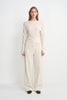 A model wearing Rue Sophie’s Talia Wide Leg Corduroy Pant in Winter White, styled with an ivory draped long-sleeve top and black square-toe shoes. The full-length view highlights the relaxed wide-leg silhouette and fine vertical corduroy texture.