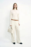 A model wearing Rue Sophie’s Talia Wide Leg Corduroy Pant in Winter White, styled with an ivory long-sleeve top, a light satin scarf around the neck, a cream handbag, and dark square-toe shoes.