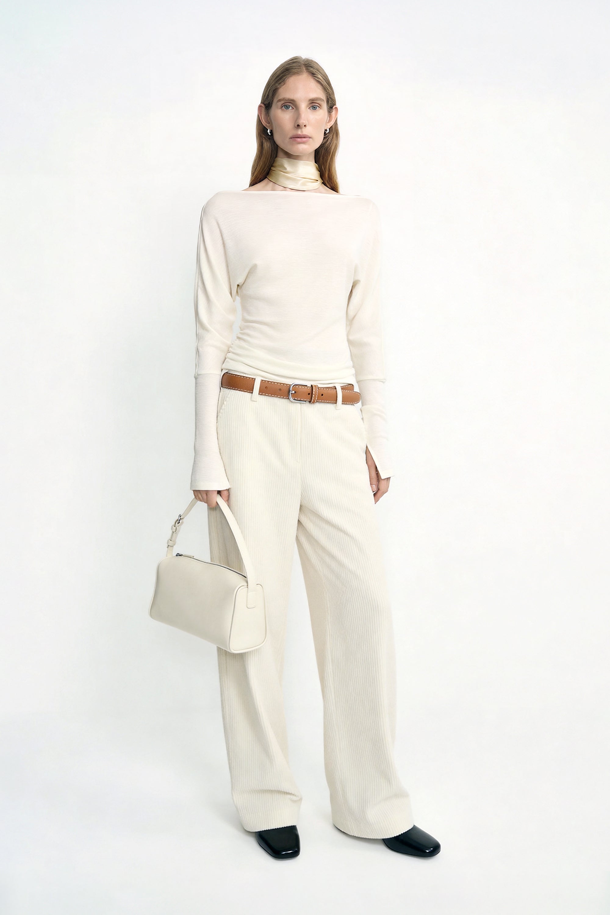 A model wearing Rue Sophie’s Talia Wide Leg Corduroy Pant in Winter White, styled with an ivory long-sleeve top, a light satin scarf around the neck, a cream handbag, and dark square-toe shoes.